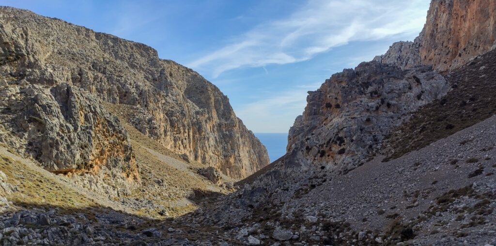 A huge descending canyon from both right and left side. In the background is a blue sea and sky with a few clouds.