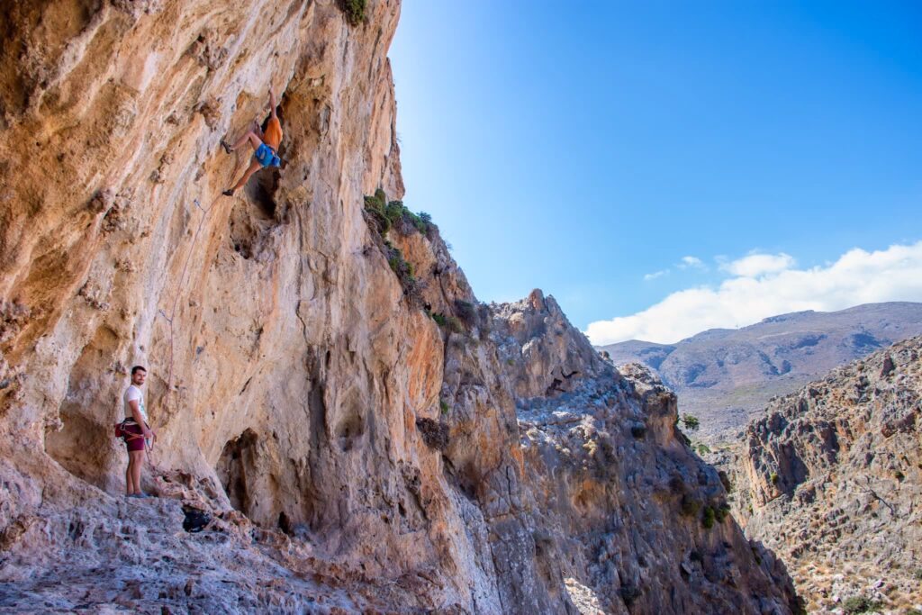 People climbing in the Katsounaki gorge, one of the best new climbing areas in the east Crete. Photo shows a big overhang with tufas and a wild landscape in the background.