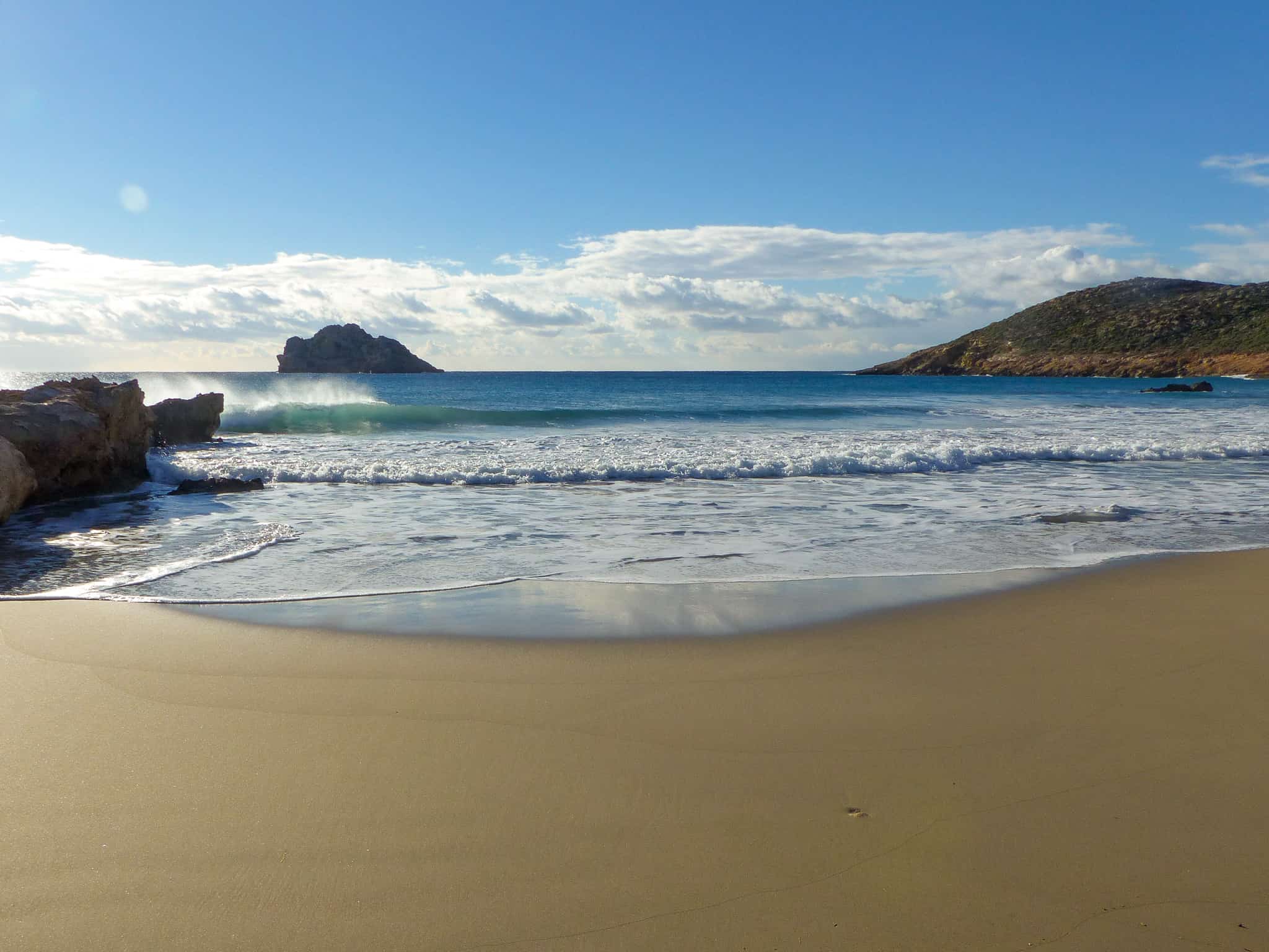 Argilos beach in Xerokampos. Yellow smooth sand and turquoise blue water. Small waves and calm sea in the back.